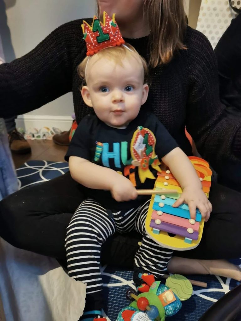 A baby playing a xylophone wearing a crown and birthday badge