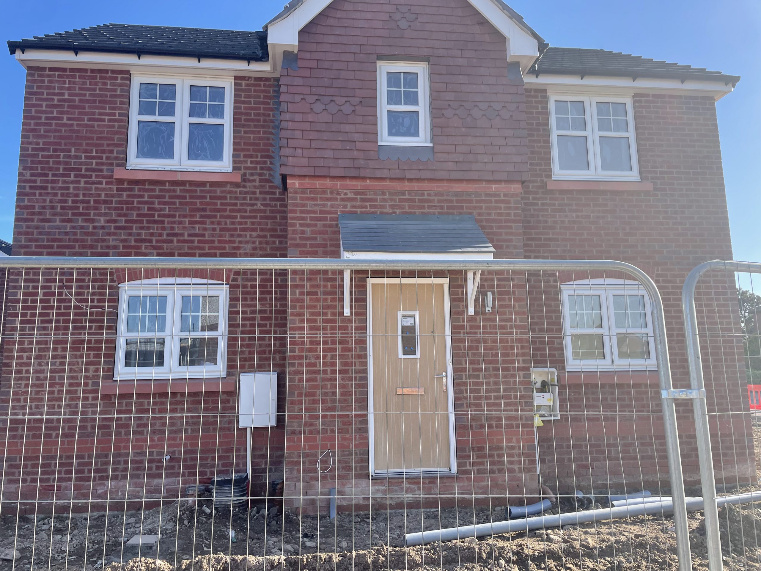 a new build detached home, with a wood coloured door and metal fencing around it