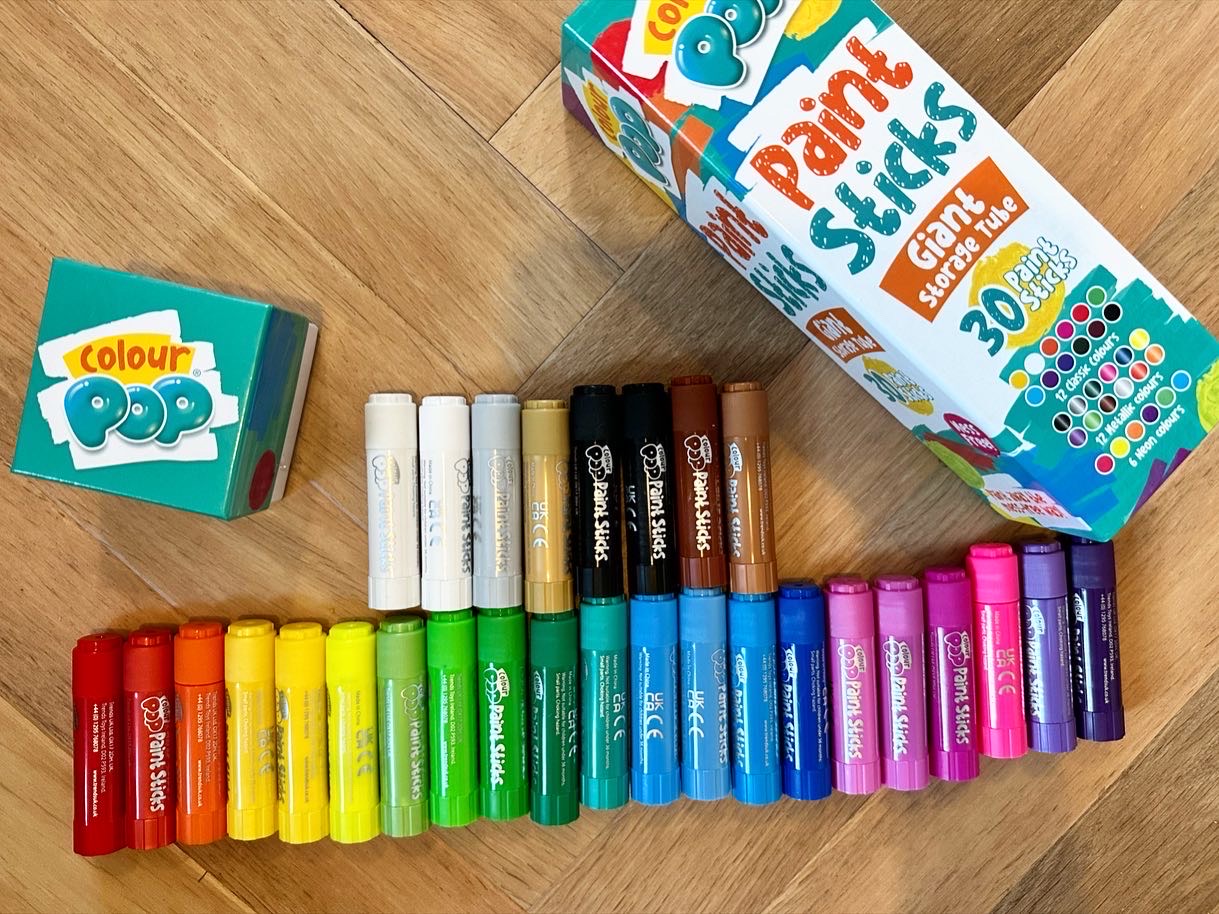 Paint sticks laid out in rainbow order with the box and lid on a wooden floor